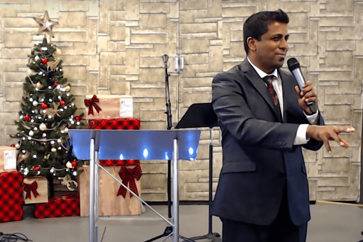 A man in a suit speaking into a microphone in front of a christmas tree.