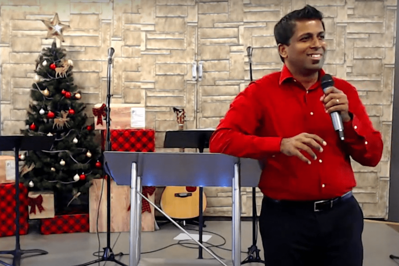 A man in a red shirt standing in front of a christmas tree.