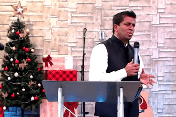 A man speaking into a microphone in front of a christmas tree.